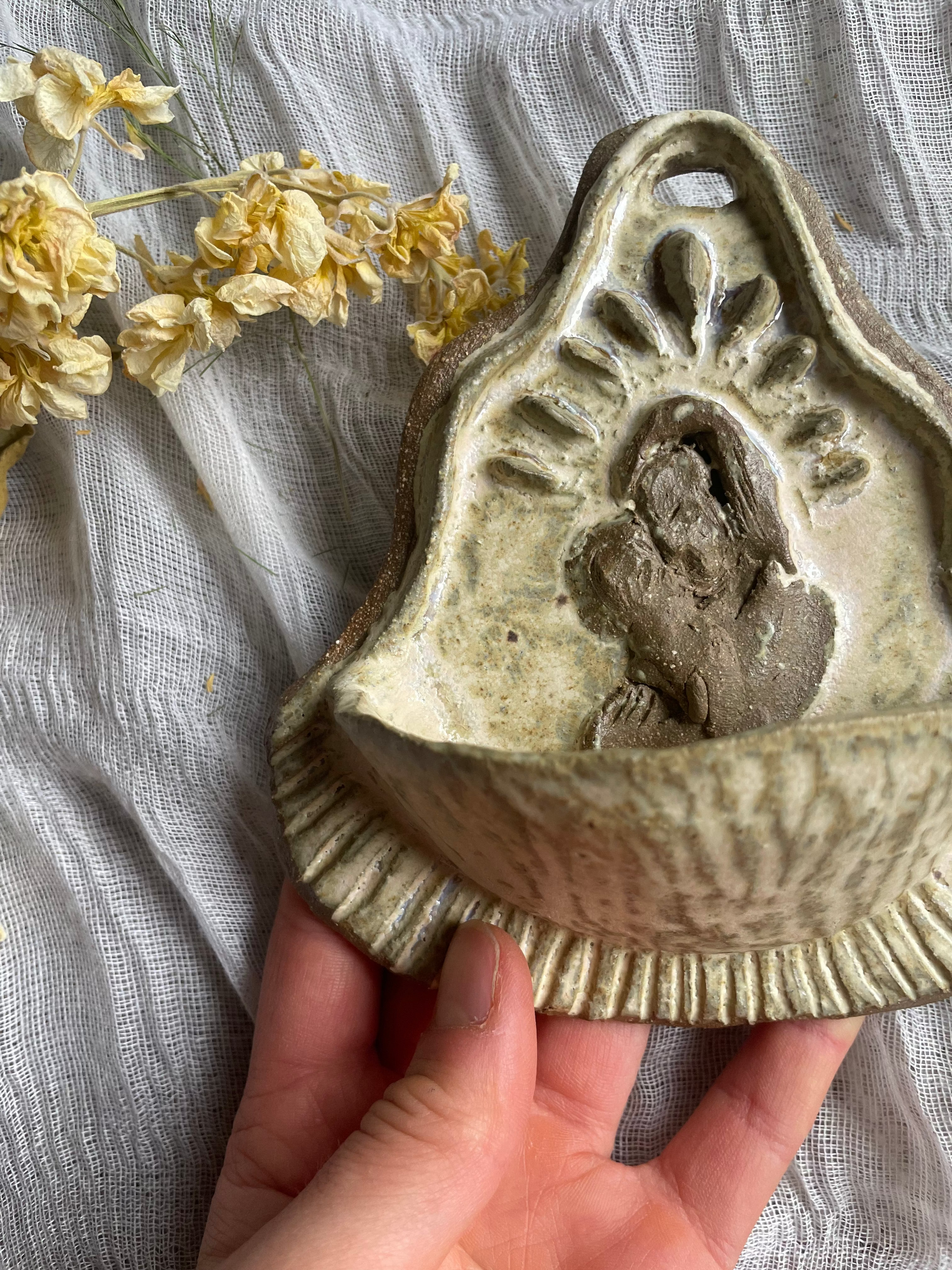 Hand holding a ceramic mold with a small figurine on a textured fabric background with yellow flowers.
